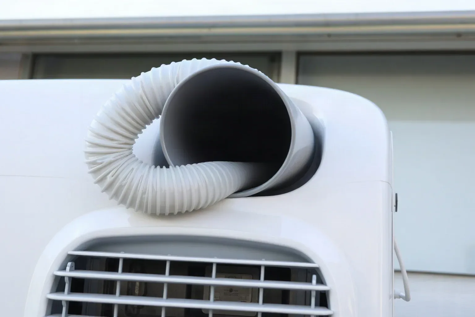 A close-up of a portable air conditioning unit with an exhaust hose venting through a slightly open window